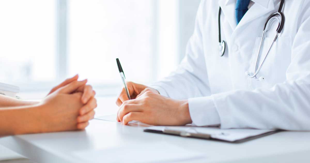 foto de um médico com caneta na mão sentado em uma mesa e paciente a frente